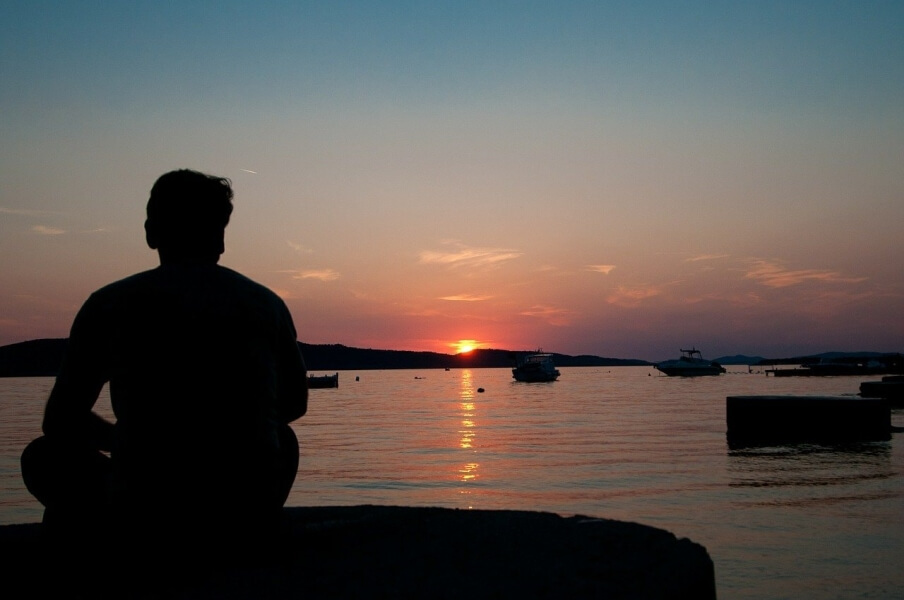 Man sitting by the beach at sunset meditating